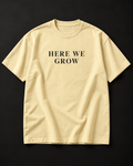HERE WE GROW heavyweight tee in buttermilk with a wide-tracked serif front print.