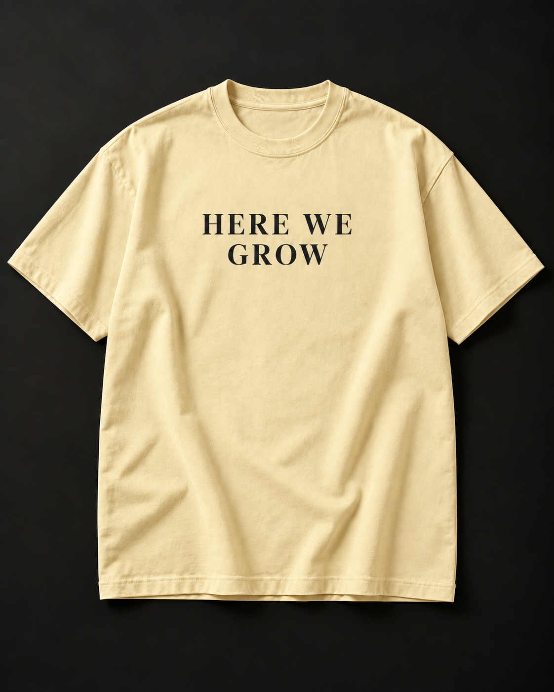 HERE WE GROW heavyweight tee in buttermilk with a wide-tracked serif front print.