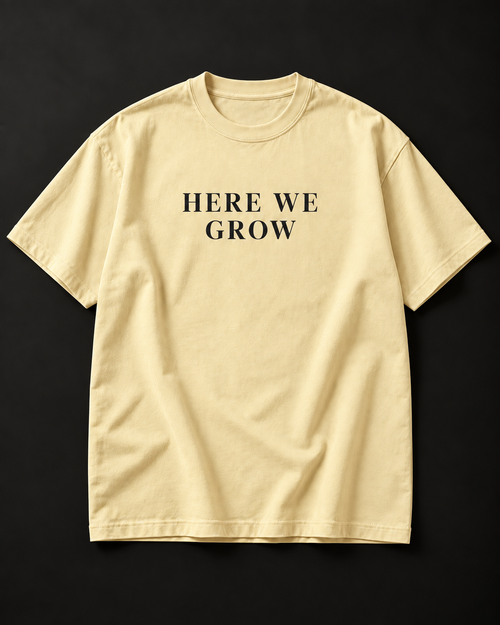 HERE WE GROW heavyweight tee in buttermilk with a wide-tracked serif front print.